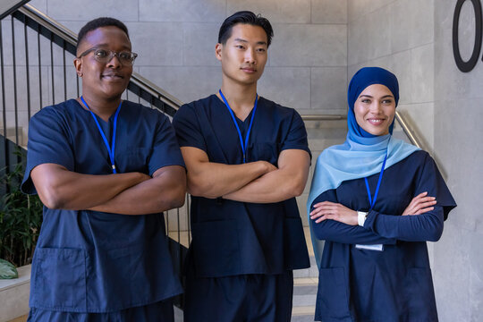 Diverse medical team standing arms crossed on clinic stairs wearing navy scrubs and blue lanyards