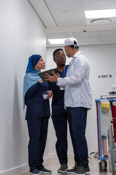 Diverse medical team wearing navy scrubs, hijab and lab coat discussing tablet near X-RAY sign