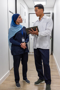 Diverse staff in scrubs and lab coat consulting over tablet with ID badge in clinic corridor