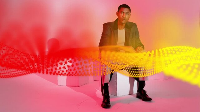 Man sitting on cube in gradient studio as red-yellow ribbon sweeping, man adjusting for design