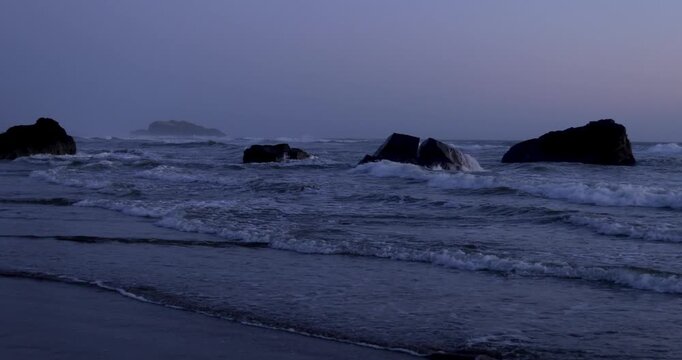 Moody ocean waves crashing on dark rocks at twilight in Oregon