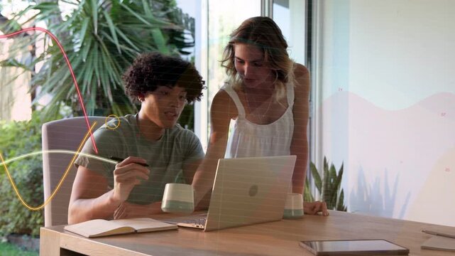Seated man tapping pen, activating waves overlaying table while woman pointing at laptop designing