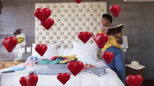 Woman reading checklist on bed urging man folding cloth by suitcase for travel, hearts drifting