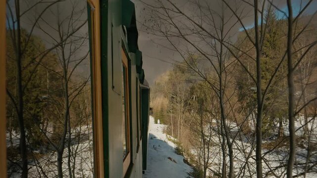 A steam train named Mocanita travels through a winter forest covered in snow. The train moves along the tracks as trees line the route on a cold day.