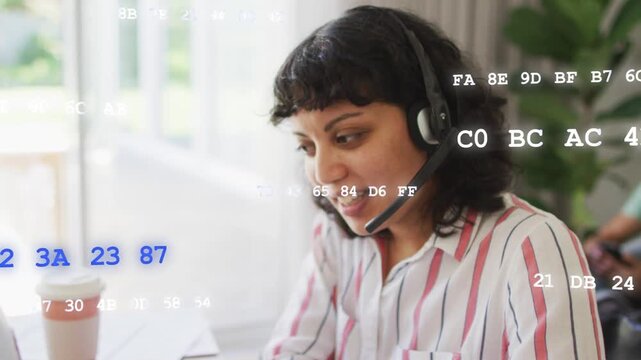Woman on headset taking tech call, leaning and typing while hex code overlaying laptop and papers