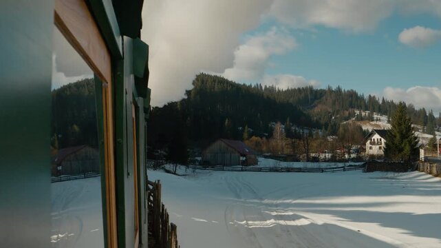 The Mocanita steam train moves through the snow-covered villages of Bucovina, Romania. Thick smoke rises as the train passes scenic landscapes and wooden houses.