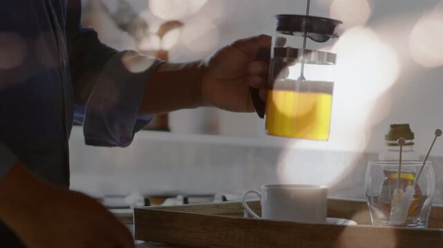 Man entering holding French press, tilting and steadying over cup in kitchen, teaching coffee prep