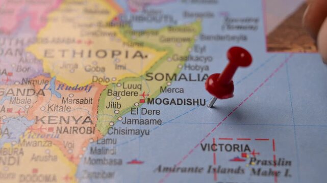 Close-Up 4K 60fps Shot: Hand Placing Red Pin on Mogadishu Location in Paper World Map Travel Concept