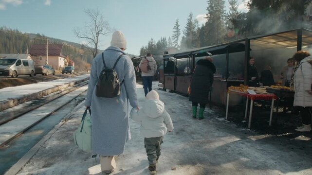 A mother and her child walk through the tourist train station in Bucovina. They pass by food stalls and enjoy the steam from nearby vendors.