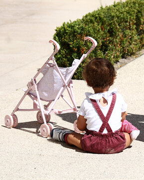 Ni&ntilde;a peque&ntilde;a infante sentada en el suelo con juguete nene child, tirantes y carrito de beb&eacute; en infancia y crecimiento y desarrollo feliz