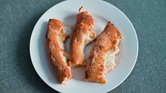 Four bread sticks are placed on a white plate on a flat surface. Pizza slices, crusts