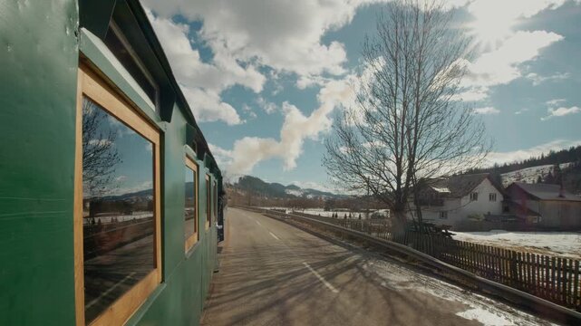 Mocanita steam train moves through Bucovina, Romania. Thick smoke rises as it journeys past villages, offering views of landscapes and rural life.