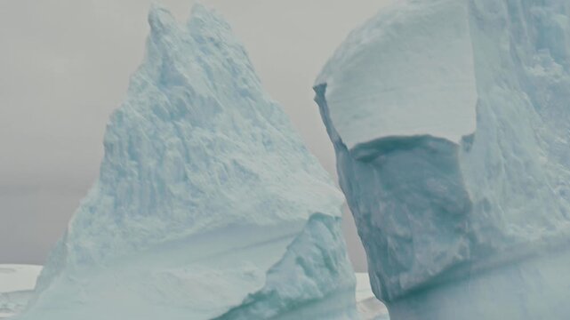 Close-up pass alongside towering sculpted Antarctic icebergs revealing dramatic blue erosion cavities and textured ice formations