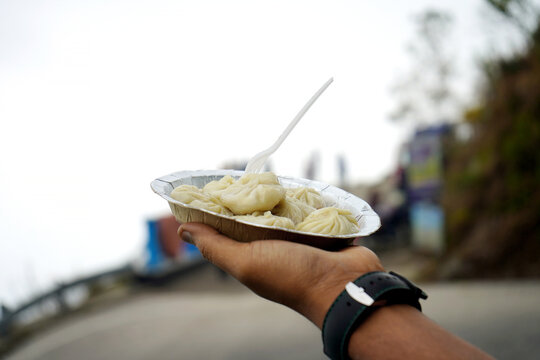 Hand holding a plate of steamed momos dumplings with a blurred mountain background