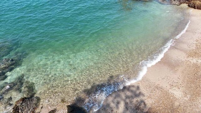 crystal clear turquoise sea water with small waves gently lapping onto a sandy pebble beach. Natural summer sunlight reflecting on the water surface. Refreshing vacation background.	
