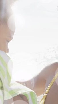 Vertical video: Mother adjusting towel, pulling child close at beach, sun rays showing family bond