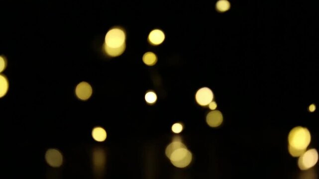 Yellow holiday bokeh lights flash actively in the dark as bright circles pulsate and move. Spots of light quickly flicker and sparkle to create an energetic holiday light pattern.