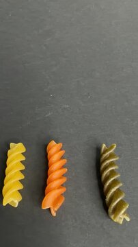 Colorful uncooked fusilli pasta spinning on a dark background. Variety of italian raw rotini pasta in green, yellow, and orange, showcasing healthy carbohydrates and italian cuisine