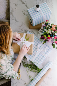 Woman wrapping gifts with ribbon and flowers on table