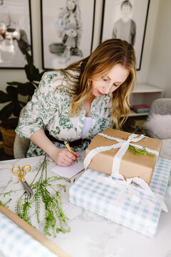 Middle aged woman writing note beside wrapped gifts at table