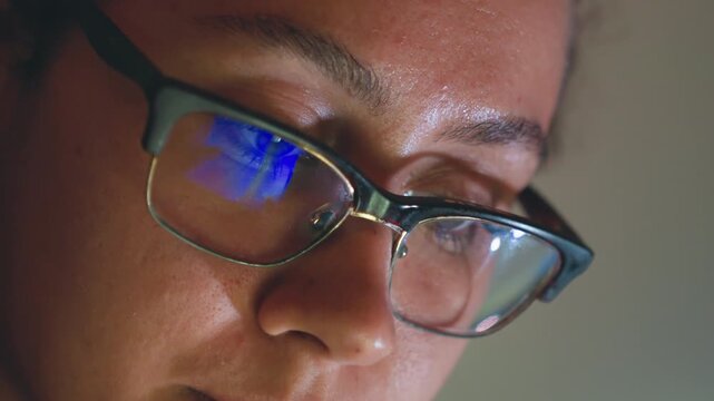 Closeup woman with glasses coding late at night, vivid blue screen reflection in lenses, concentrated expression with beads of sweat, keyboard typing and rapid debugging, startup urgency and deadline