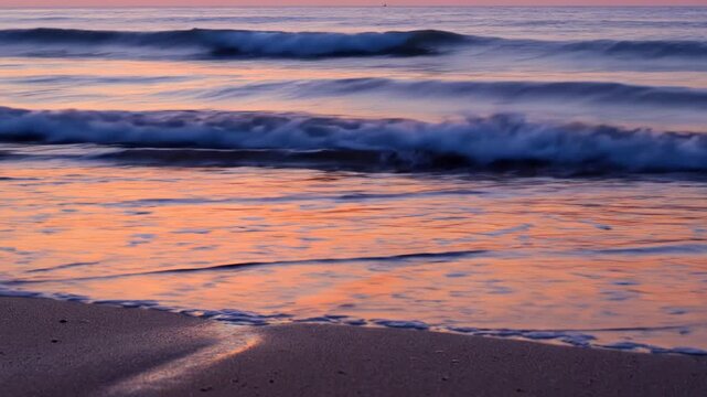 Serene sunset over the ocean with gentle waves washing onto the sandy beach