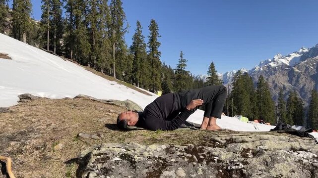 man practicing wheel pose yoga on mountain with snow and pine forest background