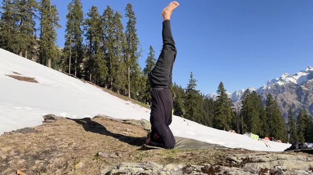 isolated yogi balancing in headstand pose on hillside with pine forest and mountain backdrop