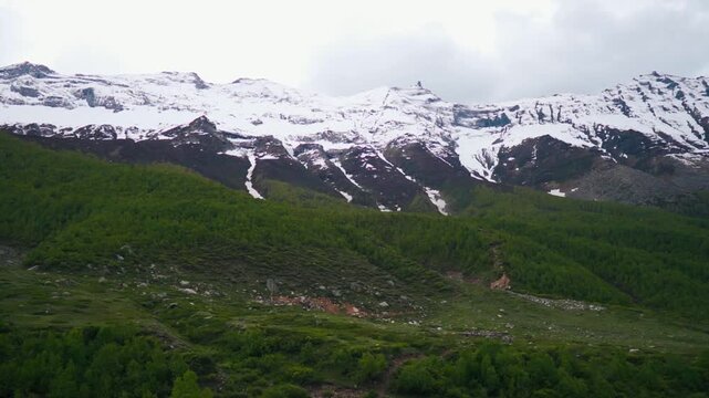 Wide angle shot of snow covered Himalayan mountain peaks with clouds above them during the summer season as seen from Sural Bhatori in Pangi Valley, Himachal Pradesh, India. Natural background.