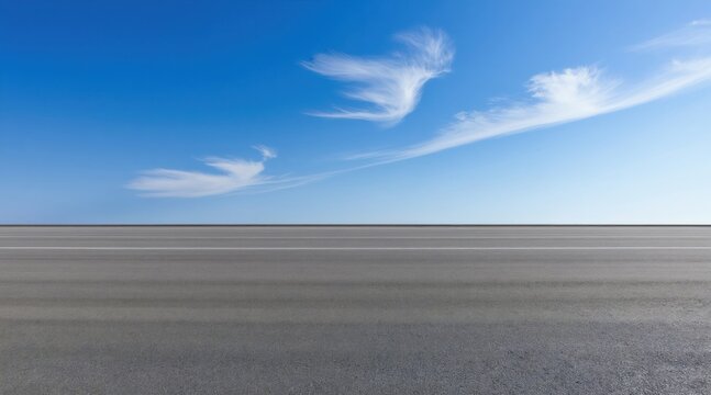 Wide empty asphalt road stretches to horizon under clear blue sky with sparse white clouds. Grayscale pavement texture offers ample copy space for design and ad concepts.