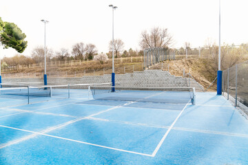 Blue pickleball court and nets on an outdoor sports facility, featuring lines, light poles, and spectator stands © Koldo_Studio