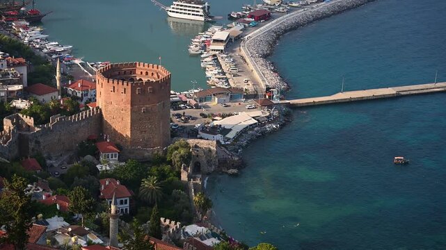 Panoramic view of Alanya harbor with Red Tower and Mediterranean sea at sunset. Historic Kizil Kule fortress in Turkey. Summer vacation, Turkish Riviera, and coastal city travel concept.
