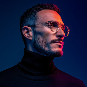 Studio portrait of a modern man wearing a black turtleneck and black glasses.