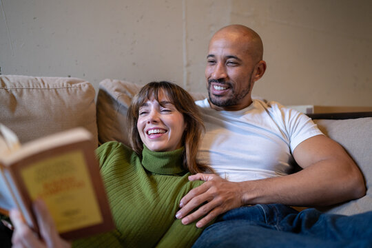 Couple relaxing on sofa reading a book together at home