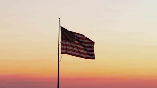 American flag waving in wind at sunset against colorful sky, captured in aerial view, symbolizing patriotism, freedom and national pride in serene evening atmosphere across USA.