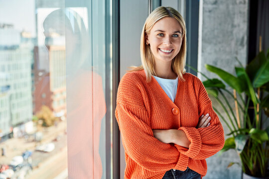 Smiling young businesswoman standing with arms crossed near window