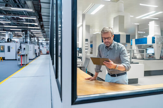 Engineer using tablet in production hall with industrial machinery