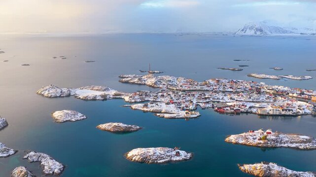 Cinematic aerial shot of the famous Henningsvaer fishing village surrounded by icy blue arctic waters and snowcapped islands in Lofoten, Norway.