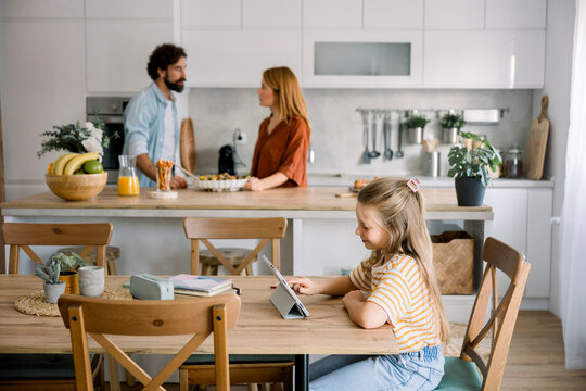 Child learning with digital tablet as parents talk in kitchen at home