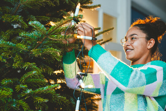 Young woman decorating Christmas tree with fairy lights