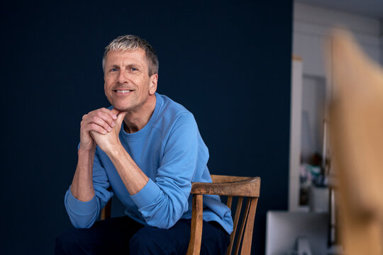 Smiling retired senior man sitting on chair at home