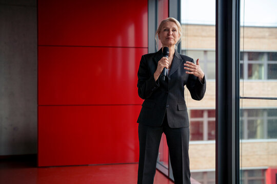 Senior public speaker holding microphone and communicating at office