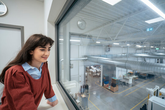 Smiling businesswoman looking out of glass window in factory