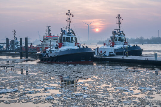 Tugboats docked in icy harbor water at sunrise in Hamburg