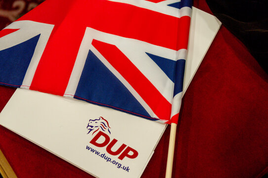A DUP party manifesto rests on a blue upholstered chair next to a small Union Jack flag, capturing the political atmosphere of a Democratic Unionist Party annual conference in Northern Ireland.