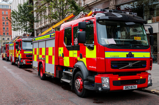 A line of modern Northern Ireland Fire and Rescue Service (NIFRS) appliances, featuring high-visibility red paint and yellow Battenburg markings, attending an emergency response.