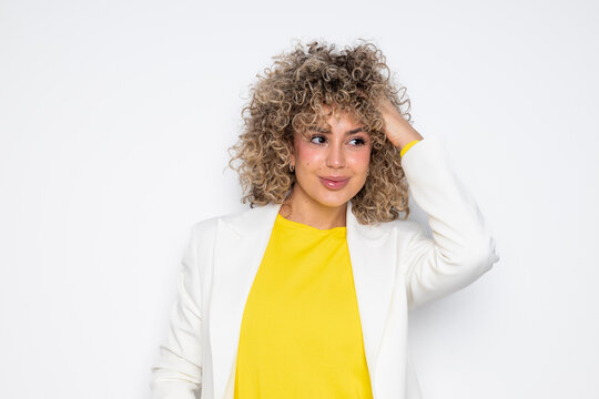 Smiling business woman with curly hair in a yellow sweater and white blazer in a studio