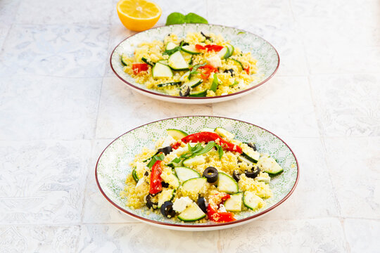 Two plates of fresh zucchini couscous salad with feta and olives