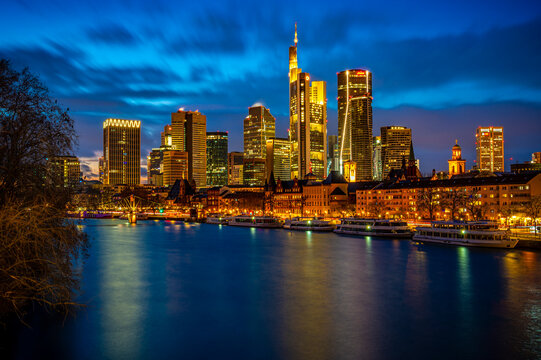 Illuminated Frankfurt am Main skyline reflecting on river at dusk
