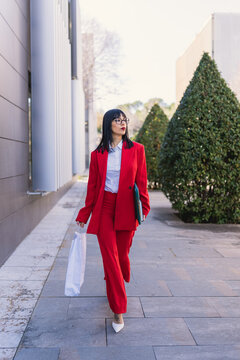 Confident businesswoman in red suit walking outdoors in the city